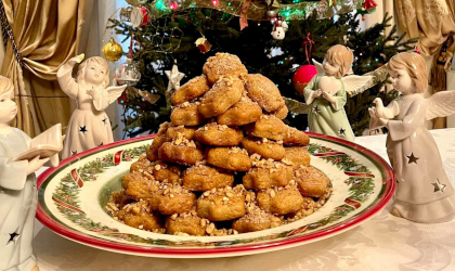 a plate piled high with brown melomakarona cookies, with angel decorations near the plate and a bit of Christmas tree in the background