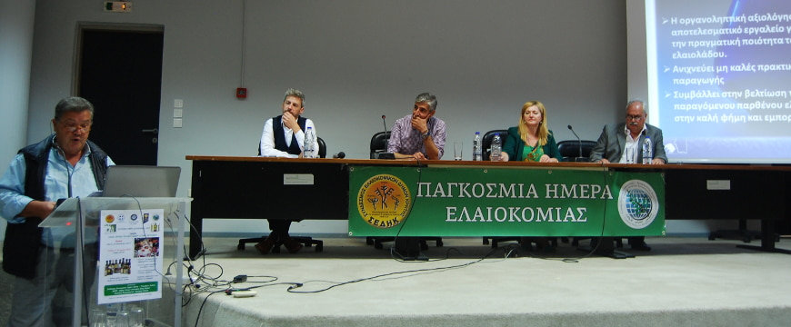 World Olive Day speakers, one standing at a podium, others sitting behind a table on a stage