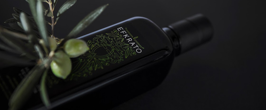 a bottle of Efkrato olive oil lying on its side with 2 olives and some leaves on a branch on the left