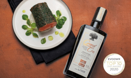 a bottle of Terra Creta Grand Cru extra virgin olive oil between a plate of delicacies and the EVOOWR Top 10 badge