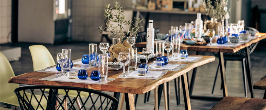 a wooden table set with blue olive oil tasting glasses and wine and water glasses on placemats