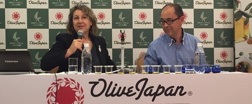 Alexandra Devarenne sitting at a table next to a man, with Olive Japan on a sign hanging down in front of the table  