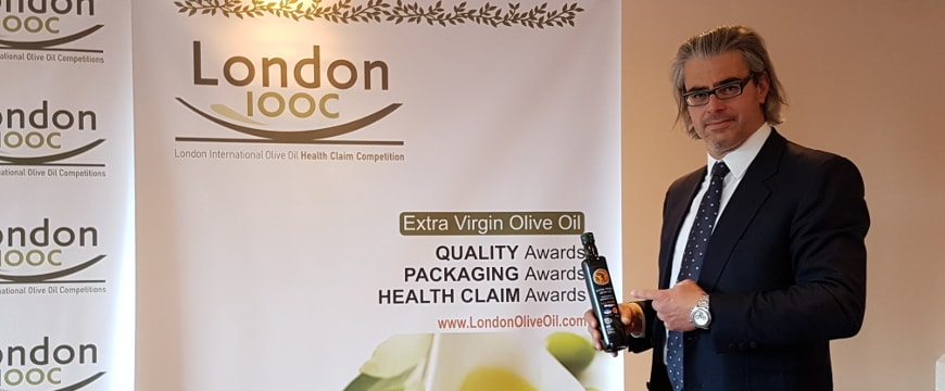Pantelis Fanourgakis with his olive oil in front of a backdrop about the London Olive Oil Competitions