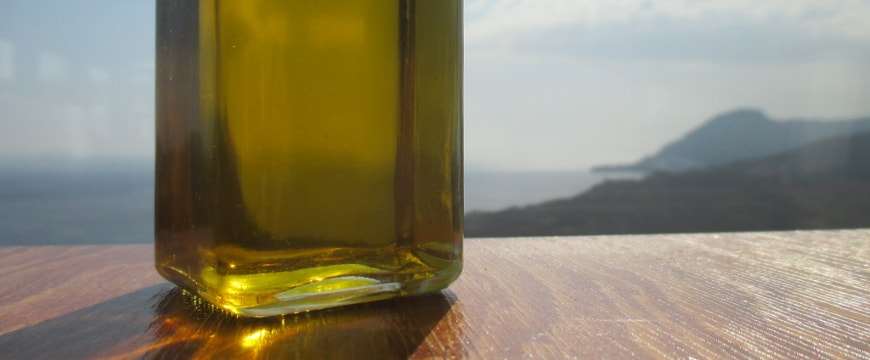 clear glass bottle with olive oil, view of sea and hills in background