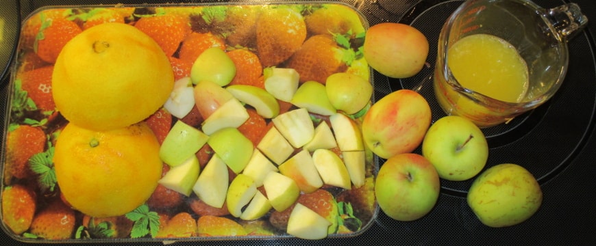 orange peel and apple chunks on a cutting board, small apples and a glass measuring cup half full of orange juice