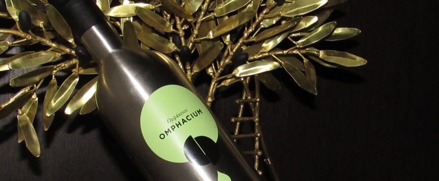 a bottle of Papadopoulos Omphacium Organic olive oil with gold olive leaves behind it