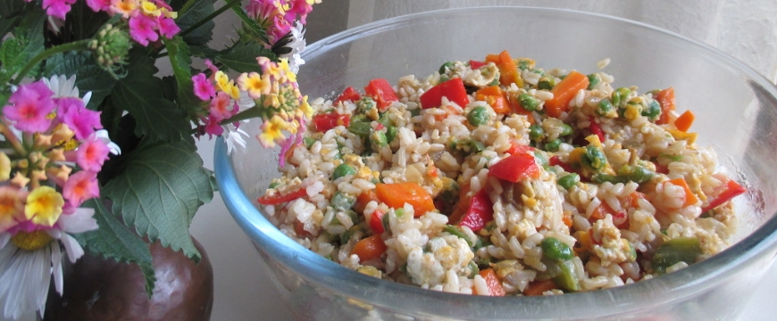 vegetable fried rice in a glass bowl next to wildflowers