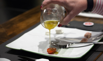 olive oil poured from a wine glass onto a small piece of tomato on a plate