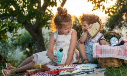 two young children having a picnic outdoors, with one of them holding a bottle of Goutis Estate olive oil