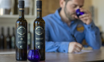 2 bottles of Laconiko olive oil in the foreground on the left, and in the background a man tasting olive oil