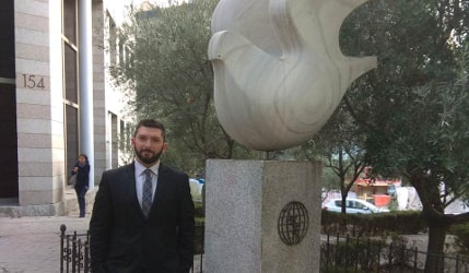 Vasilis Pyrgiotis standing next to International Olive Council symbols, a globe with an olive branch under a sculpture of a bird