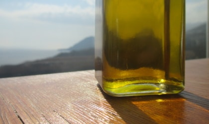 the bottom of a clear bottle of olive oil on a wooden tablel, with a sea view beyond it