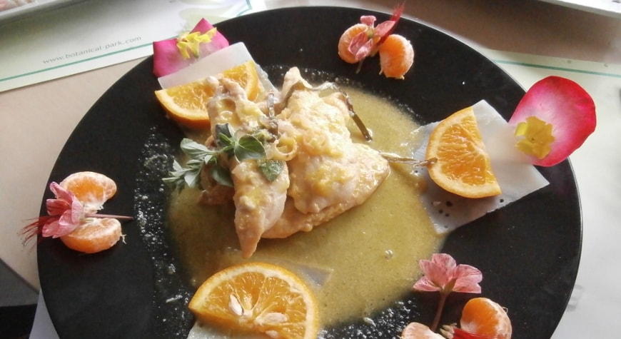 Black plate with chicken, orange slices, mandarin orange sections, and rose petals