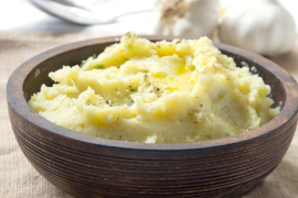 a dark bowl of mashed potatoes, with heads of garlic behind it