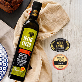 a bottle of Terra Creta olive oil lying on its side on a napkin, with New York and Berlin International Olive Oil Competition gold award logos to the right of it
