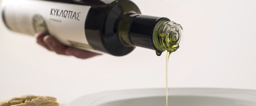 a thin stream of olive oil pouring out of a Kyklopas brand bottle