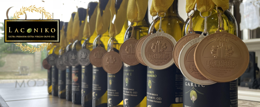 11 bottles of olive oil in a row with medals from the Los Angeles international olive oil competition around each bottle, and the Laconiko logo in the top left corner