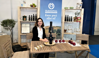 Marianna Devetzoglou sitting at a table with olive oil bottles and tasting glasses at the Food Expo