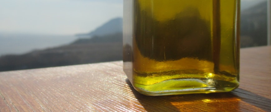 the bottom of a clear bottle of olive oil on a wooden tablel, with a sea view beyond it