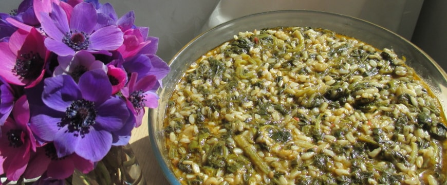 a large glass bowl of spanakorizo next to a small bouquet of anemones