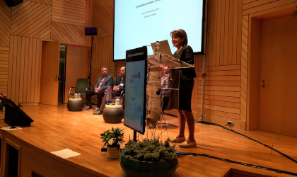 Dr. Antonia Trichopoulou standing at a podium with a panel of speakers on a stage