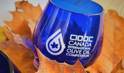 A blue olive oil tasting glass with the competition name and logo, on red maple leaves