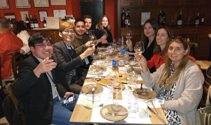 People at a long table at a winery, holding up wine glasses for a toast