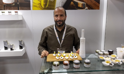 a man sitting behind a table with small appetizers for tasting olive oil, and bottles of different olive spreads