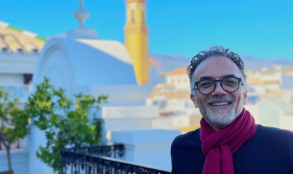 Dr. Tassos Kyriakides, with picturesque Mediterranean buildings behind him