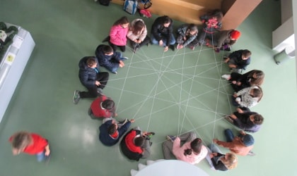 children sitting in a circle with a web of string between them, viewed from above