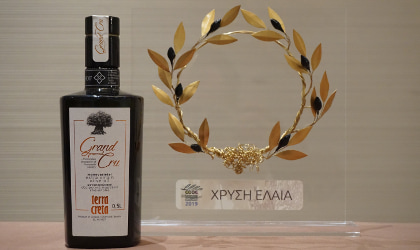 A bottle of Terra Creta Grand Cru EVOO next to a gold olive wreath, its award from the Cretan Olive Oil Competition