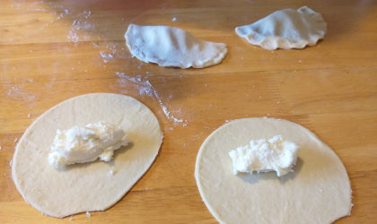 2 circles of dough with cheese filling in the middle, and two half circle raw cheese pies that have had the dough folded over and sealed
