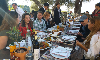 people sitting at a long table outdoors, happily conversing, with food in front of them