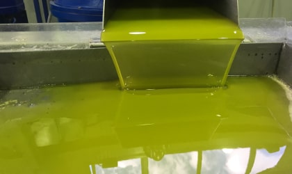 Olive oil flowing into a vat, with blue sky and clouds reflected in the oil