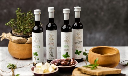 4 bottles of Pellas Nature infused olive oils on a table with bowls of olives, cheese, and herbs