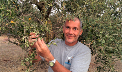 Giovanni Bianchi holding a large olive branch full of olives, in front of an olive tree