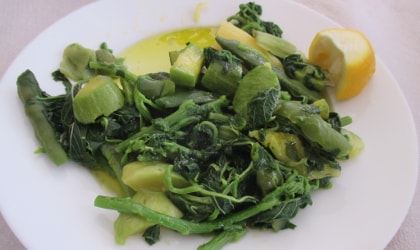 Boiled greens with olive oil and lemon on a white plate