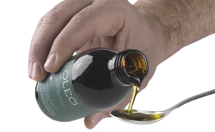 Hand pouring a spoonful of OLEO olive oil from a medicine bottle