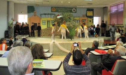 Children onstage in front of an audience, with some dancing around a giant olive 