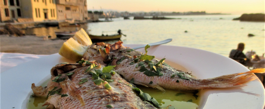 two whole fish on a plate of olive oil, with the sea in the background