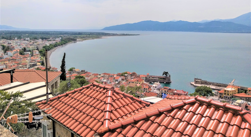 red tiled rooftops, the curve of the coastline, the Gulf of Corinth, and mountains in the distance, viewed from above Nafpaktos