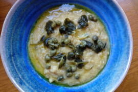 Bright blue bowl of fava with caper leaves, berries, and oil in it